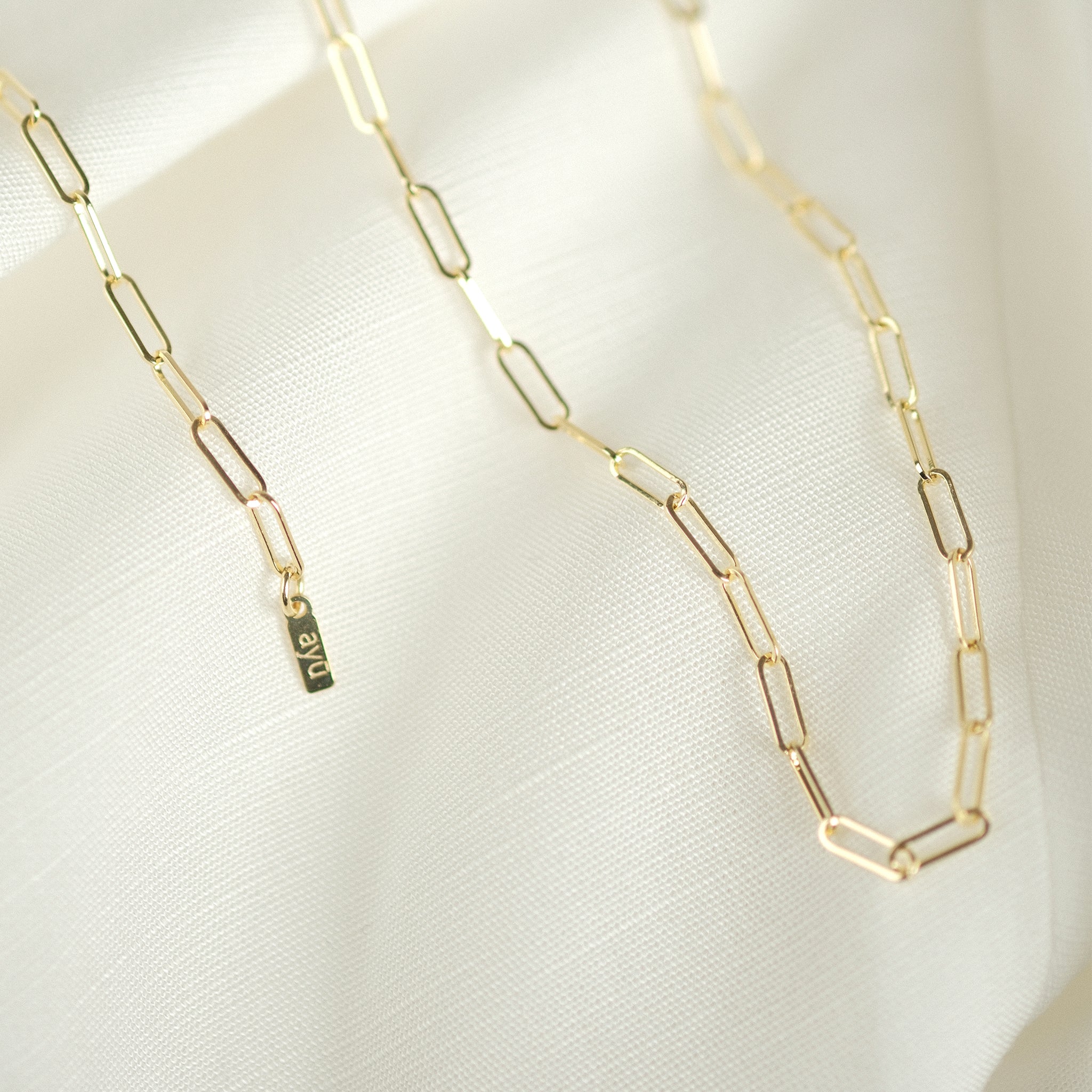 Elegante Paperclip-Kette aus 14k Gold, drapiert auf weißem Stoff, ideal als Geschenk.