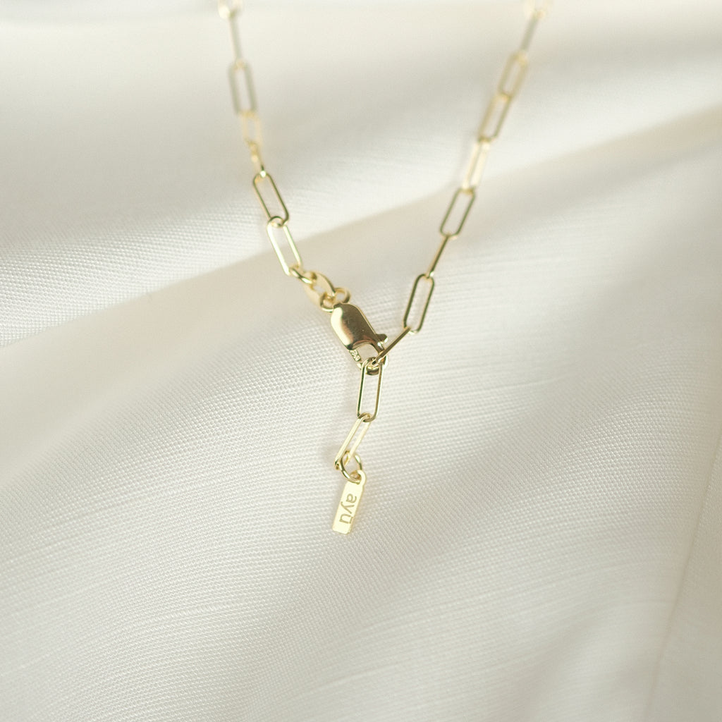 Detailansicht Verschluss: Elegante Paperclip-Kette aus 14k Gold, liegend auf weißem Stoff.