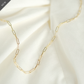 Elegante Paperclip-Kette aus 14k Gold, flach liegend auf weißem Stoff.