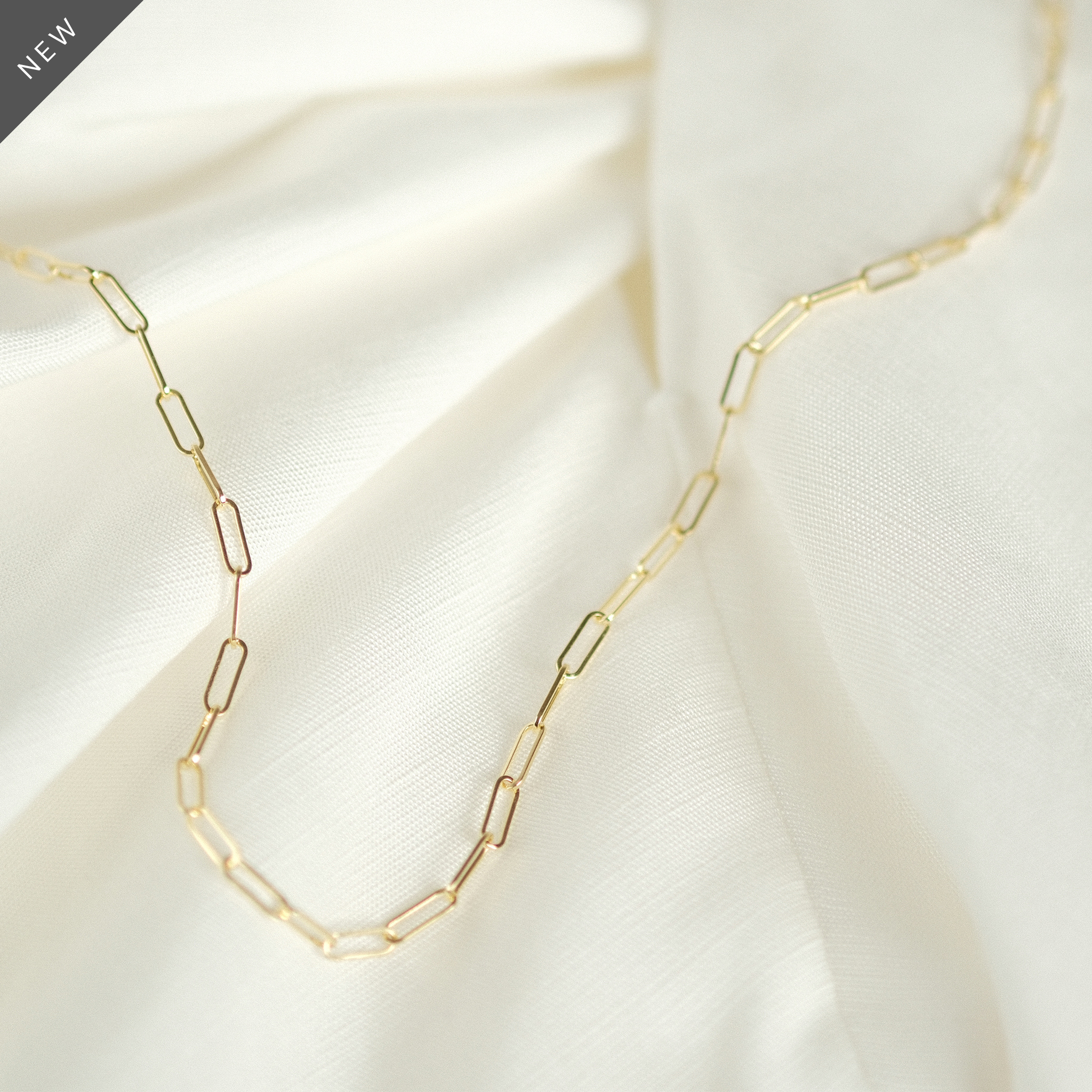 Elegante Paperclip-Kette aus 14k Gold, flach liegend auf weißem Stoff.
