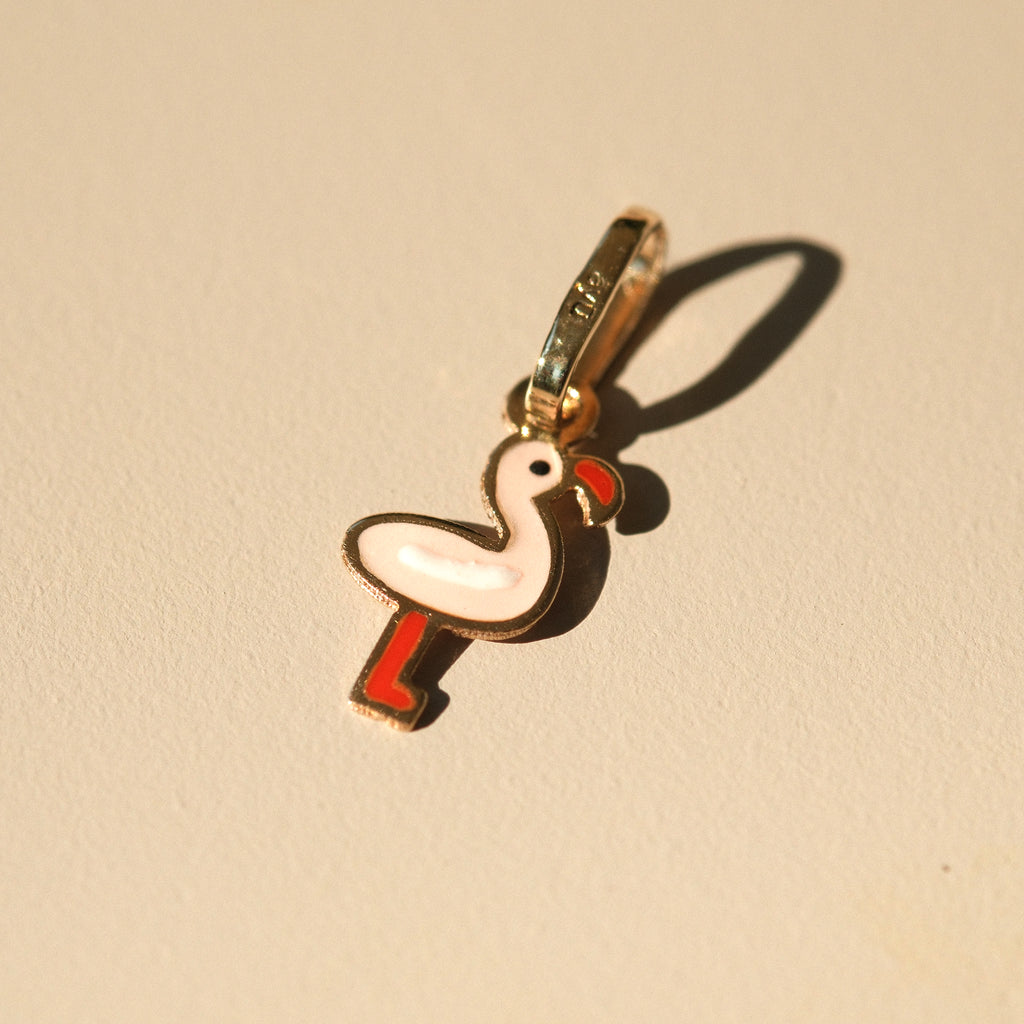 Flamingo-Anhänger aus 14k Massivgold und Emaille auf beigem Hintergrund mit Schatten.