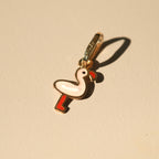 Flamingo-Anhänger aus 14k Massivgold und Emaille auf beigem Hintergrund mit Schatten.