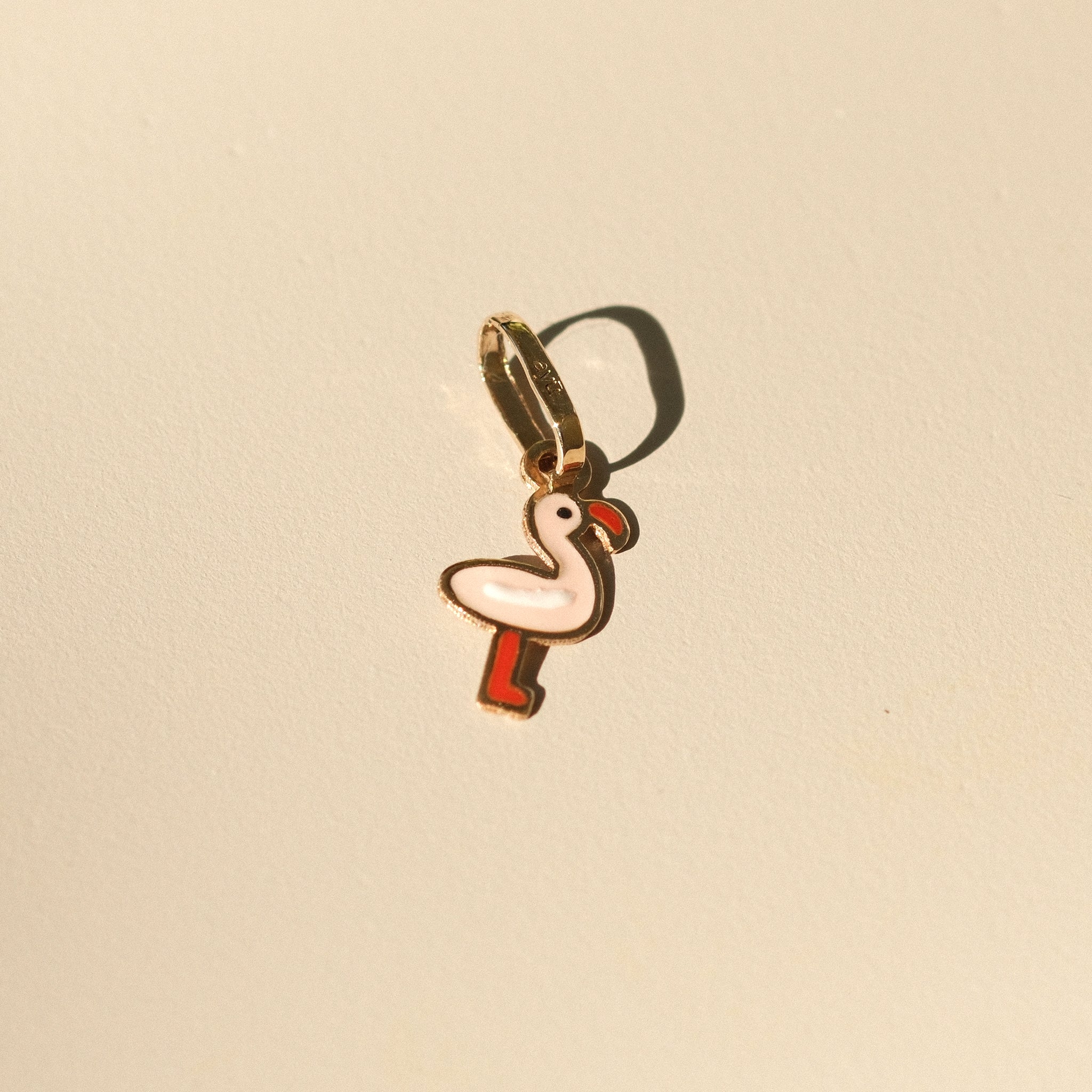 Flamingo-Anhänger aus 14k Massivgold mit rosa und roter Emaille auf beigem Hintergrund.