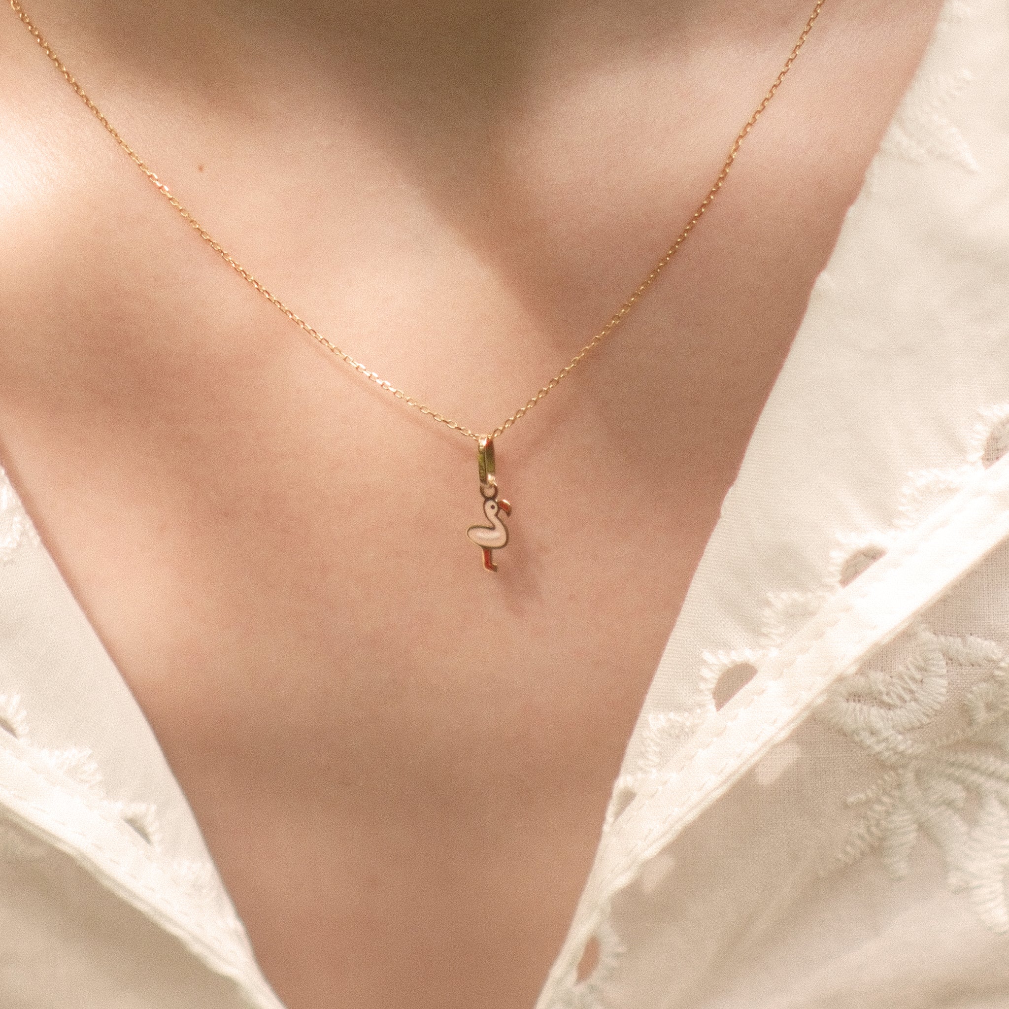 Flamingo-Anhänger aus 14k Massivgold an filigraner Goldkette getragen zu weißer Spitzenbluse.