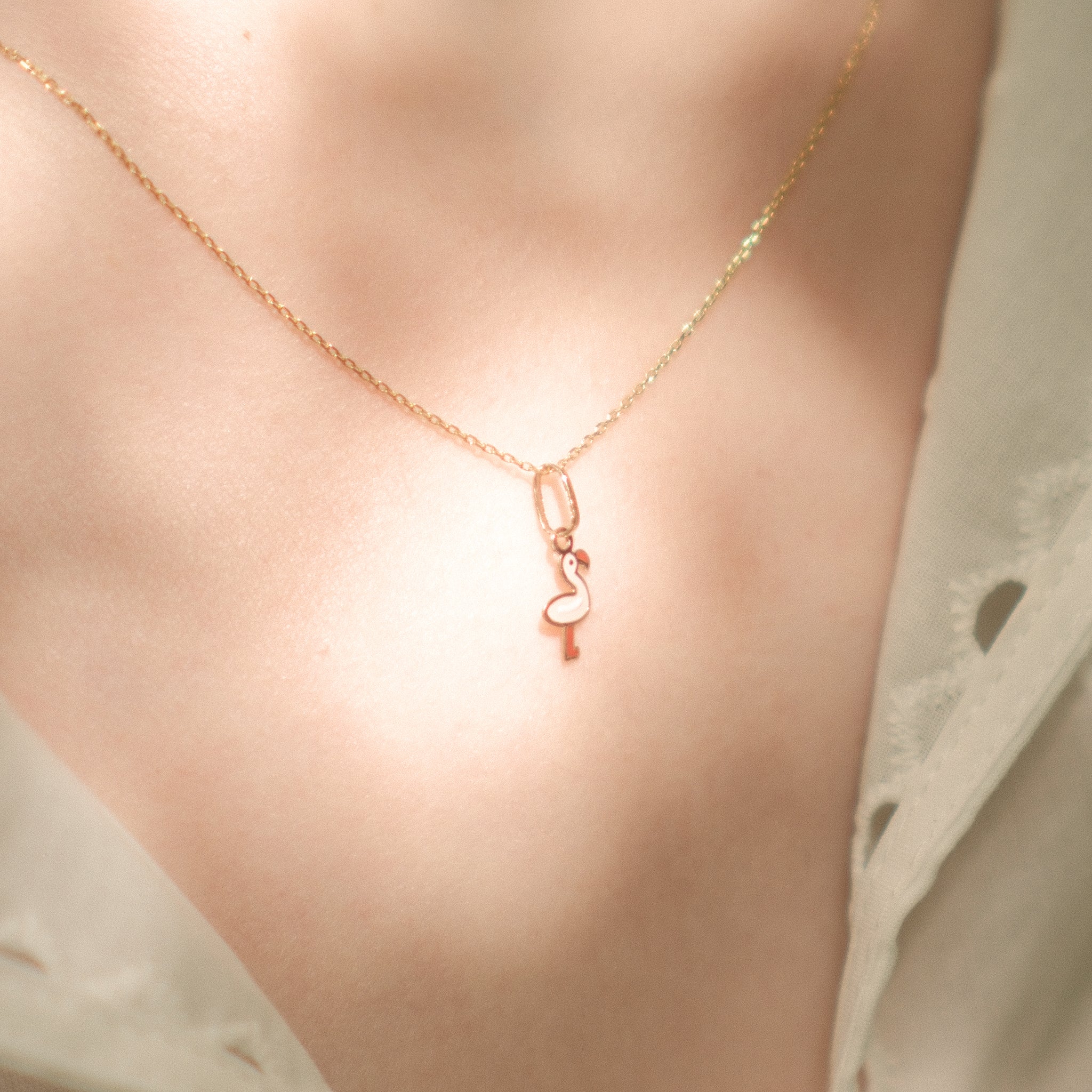 Flamingo-Anhänger aus 14k Massivgold an einer feinen Kette getragen im sommerlichen Licht.